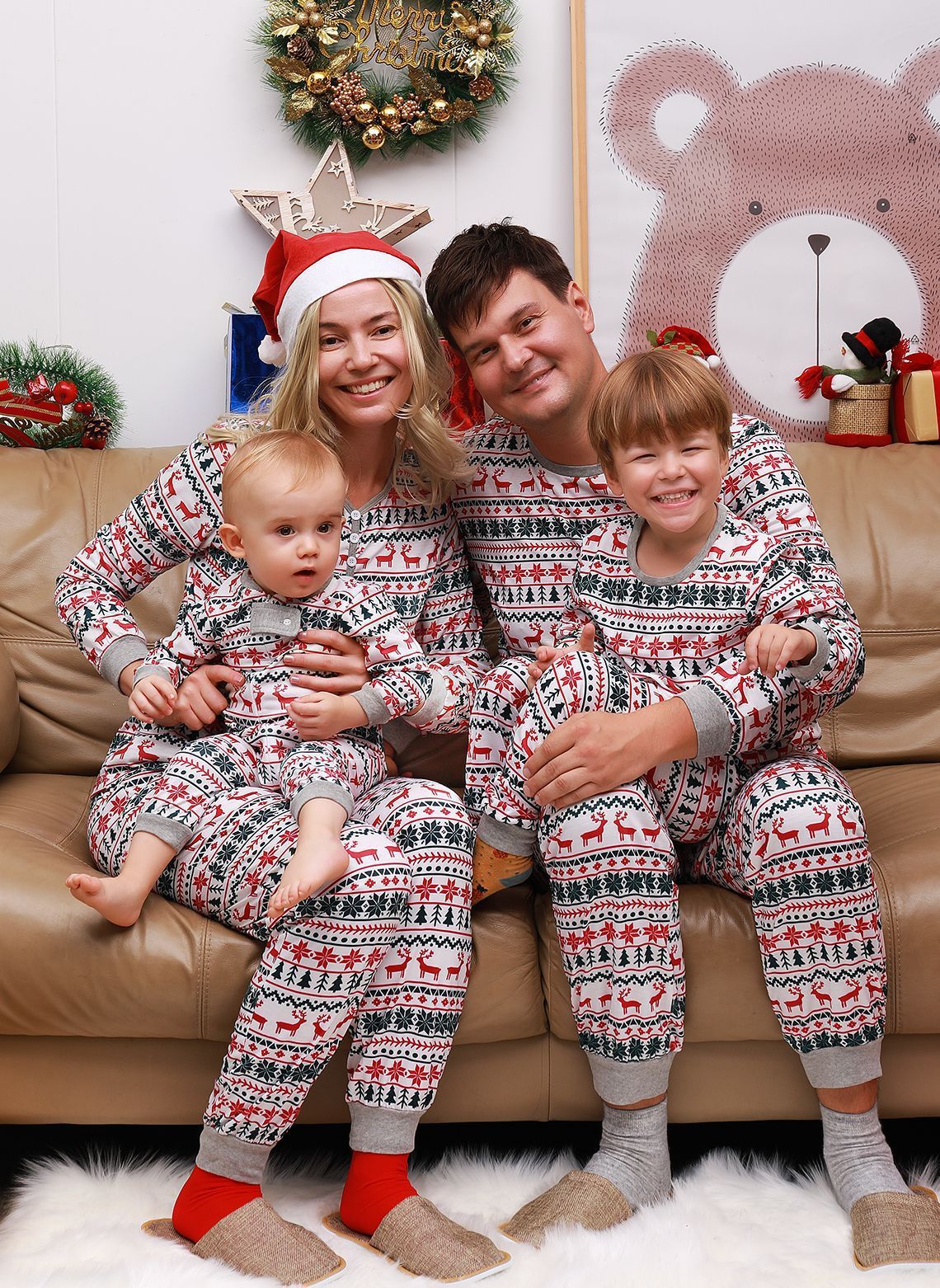 Family in matching Christmas pajama set with reindeer print and red Santa hat, sitting on couch