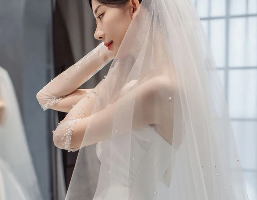 White beaded wedding dress bodice with sheer veil and elbow-length sleeves, close-up