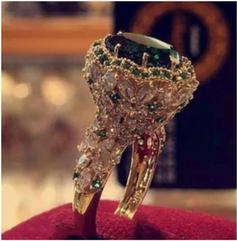 Gold-tone diamond-style ring with dark blue oval center and green accents on band.
