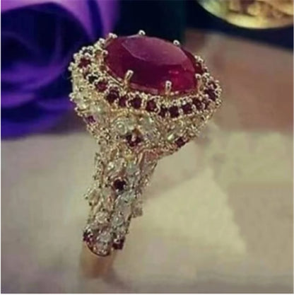 Gold-tone diamond-style ring with maroon oval center stone and scalloped halo.