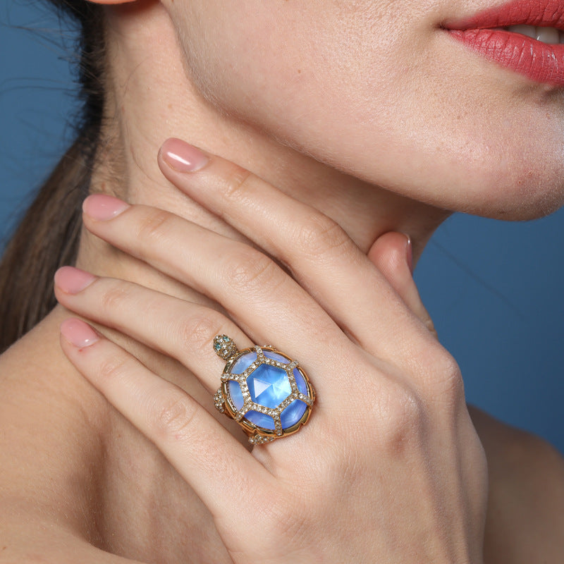 Gold turtle-style ring with round blue center stone and bezel-set clear crystals
