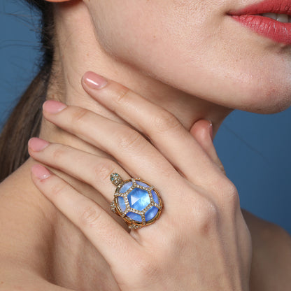 Gold turtle-style ring with round blue center stone and bezel-set clear crystals