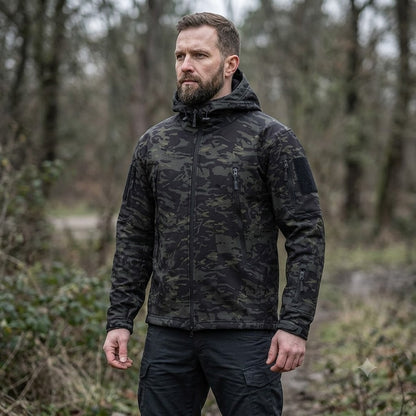 Men's dark camo tactical jacket with hood and front zipper, worn with long sleeves