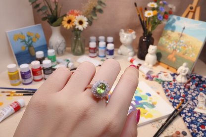 Oval peridot ring with clear-stone halo in silver-gilt, centered on open palm